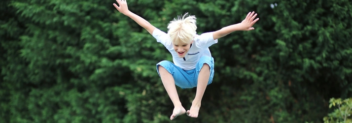 A child with light-colored hair is mid-air, arms extended outward and legs bent upward, appearing to jump or leap.